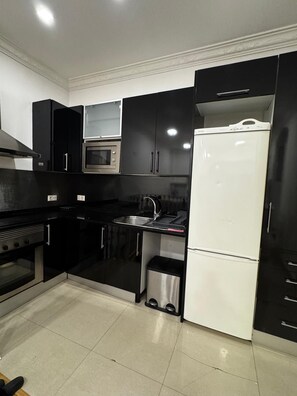 Eine Küche mit schwarzen Schränken, einem Edelstahlbackofen, einer Mikrowelle, einem Spülbecken und einem weißen Kühlschrank.