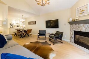 A living room with a fireplace, a television, and a dining area. - Renovated Blackcomb Townhome with Private Hot Tub & Easy Ski Access (Whistler)