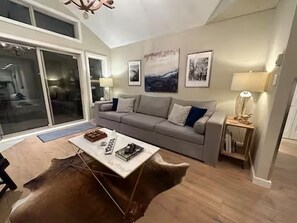 Ein Wohnzimmer mit einer Couch, einem Couchtisch und einer Lampe. An den Wänden hängen gerahmte Bilder.