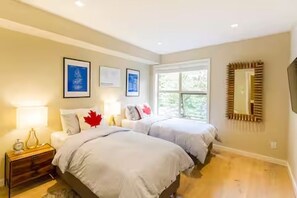 A bedroom with two beds, a nightstand, a mirror, and framed pictures on the wall. - Renovated Blackcomb Townhome with Private Hot Tub & Easy Ski Access (Whistler)