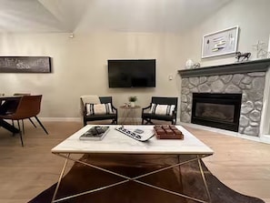 Ein Wohnzimmer mit Flachbildfernseher an der Wand, einem Kamin aus Stein und einem Couchtisch mit Zeitschriften.