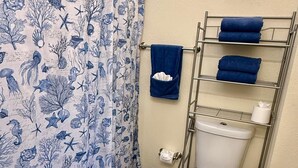 Casa de banho com cortina de chuveiro estampada com vida marinha, sanita, porta-toalhas com toalhas dobradas e um lixo.