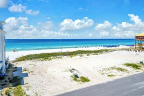 A beach with a clear sky, a sandy shore, and a building with a yellow roof. - Beach Views-Private Pool-Central PCB (Panama City Beach)