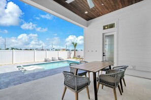 A poolside area with a table and chairs, a wooden ceiling, and a view of the sky. - Beach Views-Private Pool-Central PCB (Panama City Beach)