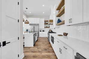 A modern kitchen with white cabinetry, a wooden floor, and built-in appliances. - Beach Views-Private Pool-Central PCB (Panama City Beach)