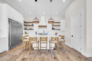 A modern kitchen with white cabinetry, a stainless steel refrigerator, wooden chairs, and pendant lighting. - Beach Views-Private Pool-Central PCB (Panama City Beach)