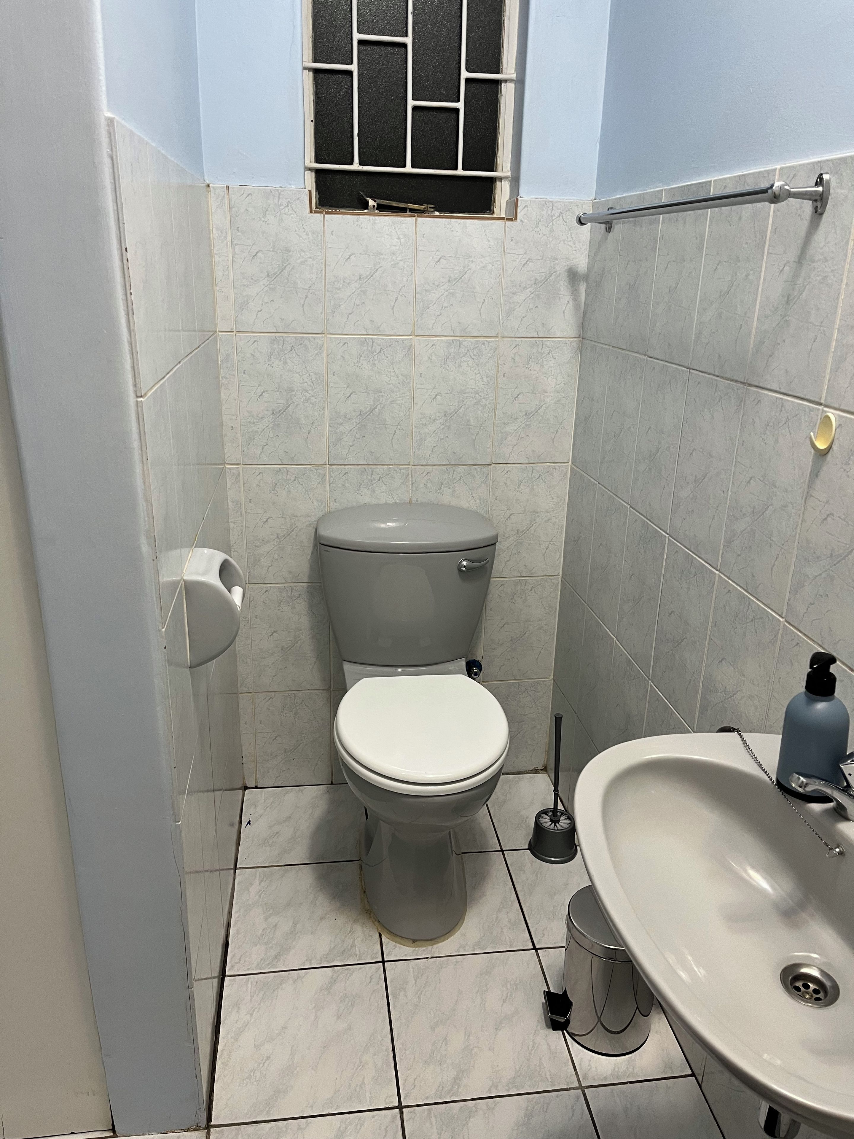 A bathroom with a toilet, sink, and a window with bars.