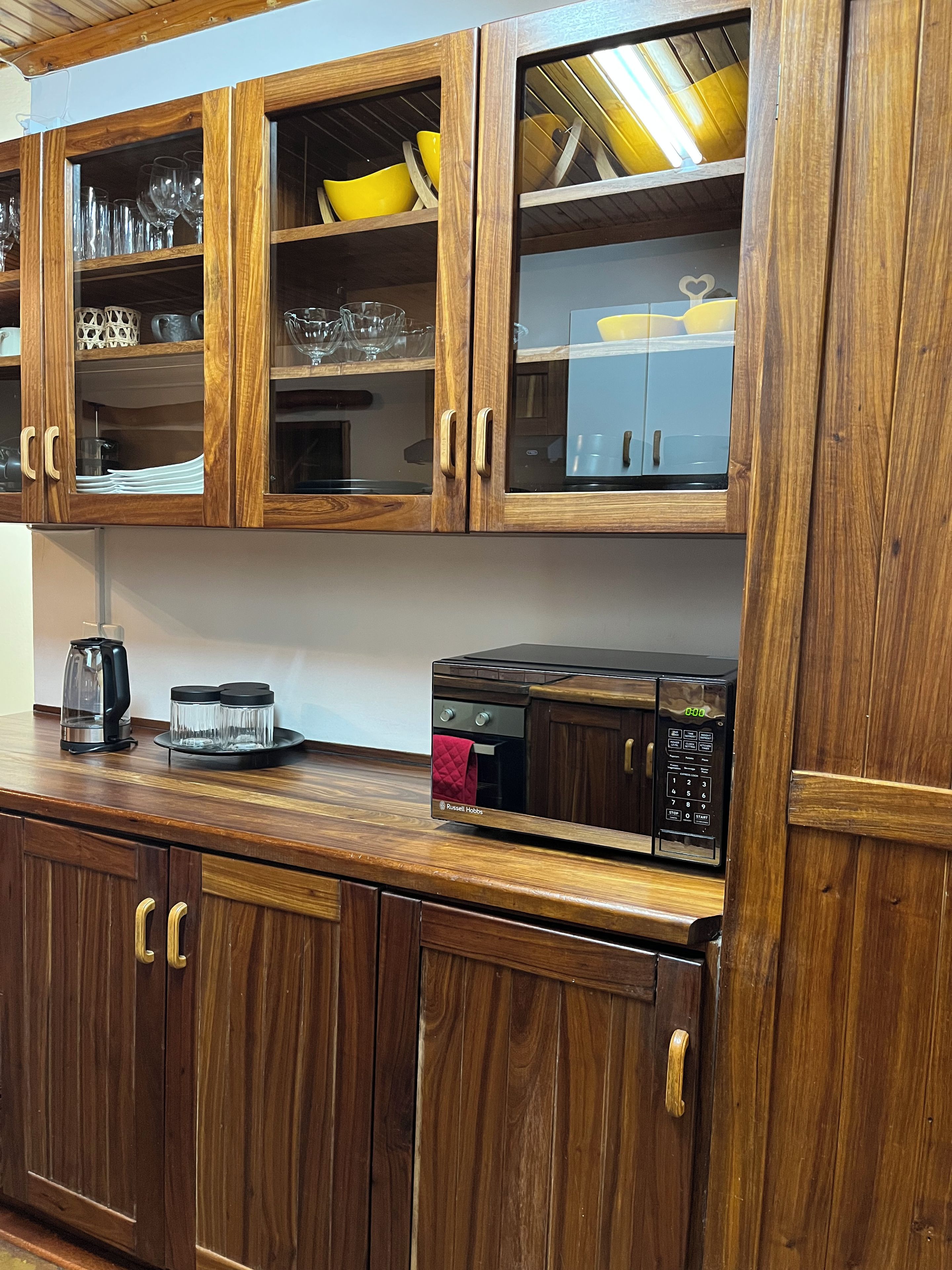 Cocina con armarios de madera, microondas, hervidor y cafetera.