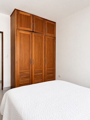 Ein Schlafzimmer mit einem großen Holzschrank und einer weißen, gesteppten Bettdecke.