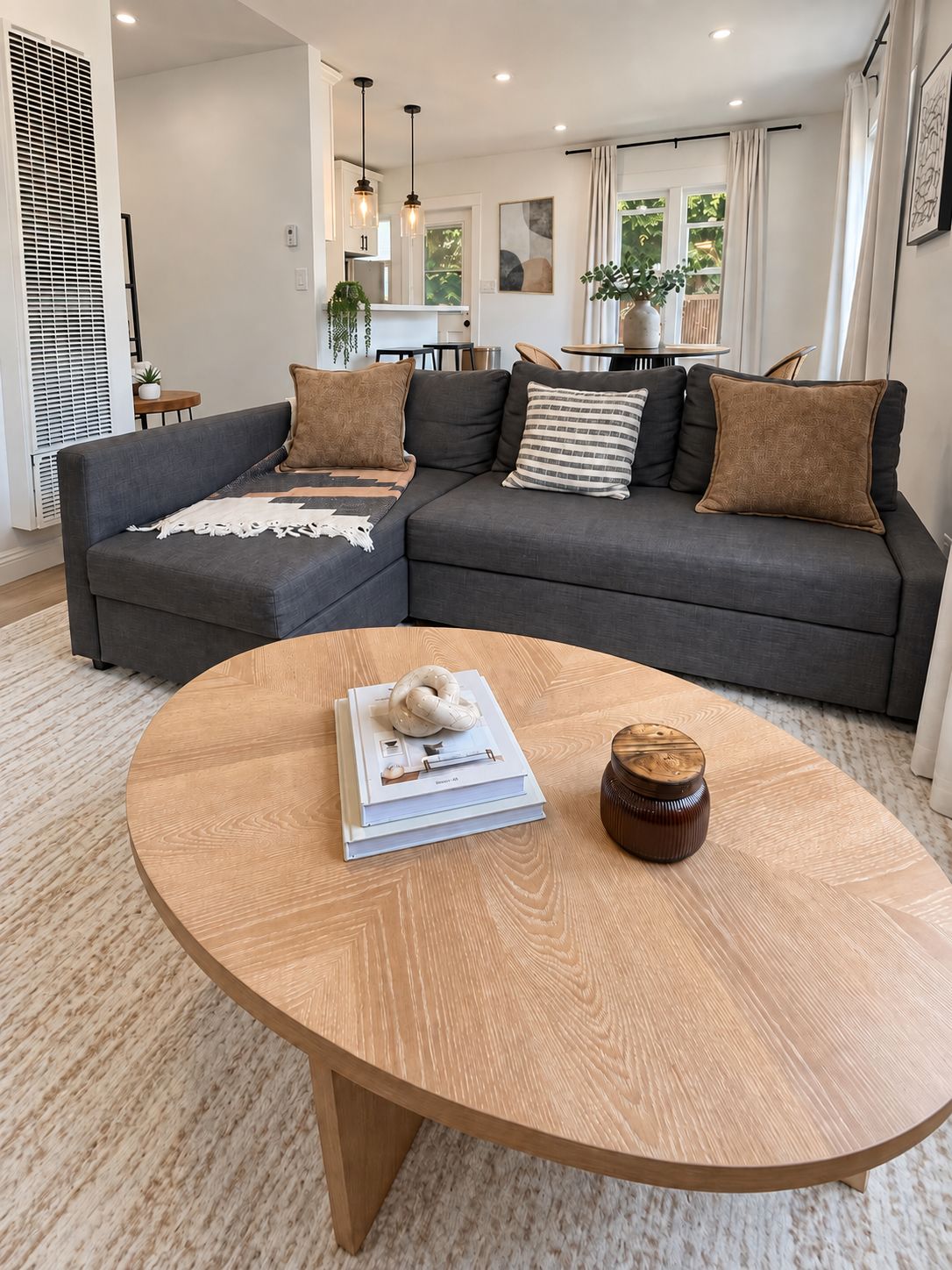 A modern living room with a sectional sofa, a wooden coffee table, and a dining area in the background.