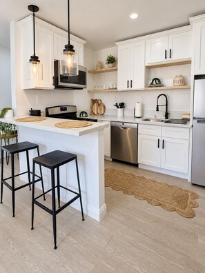 A modern kitchen with white cabinetry, a stainless steel dishwasher, and a central island with stools. - Stylish & Serene Culver City Getaway (Culver City)