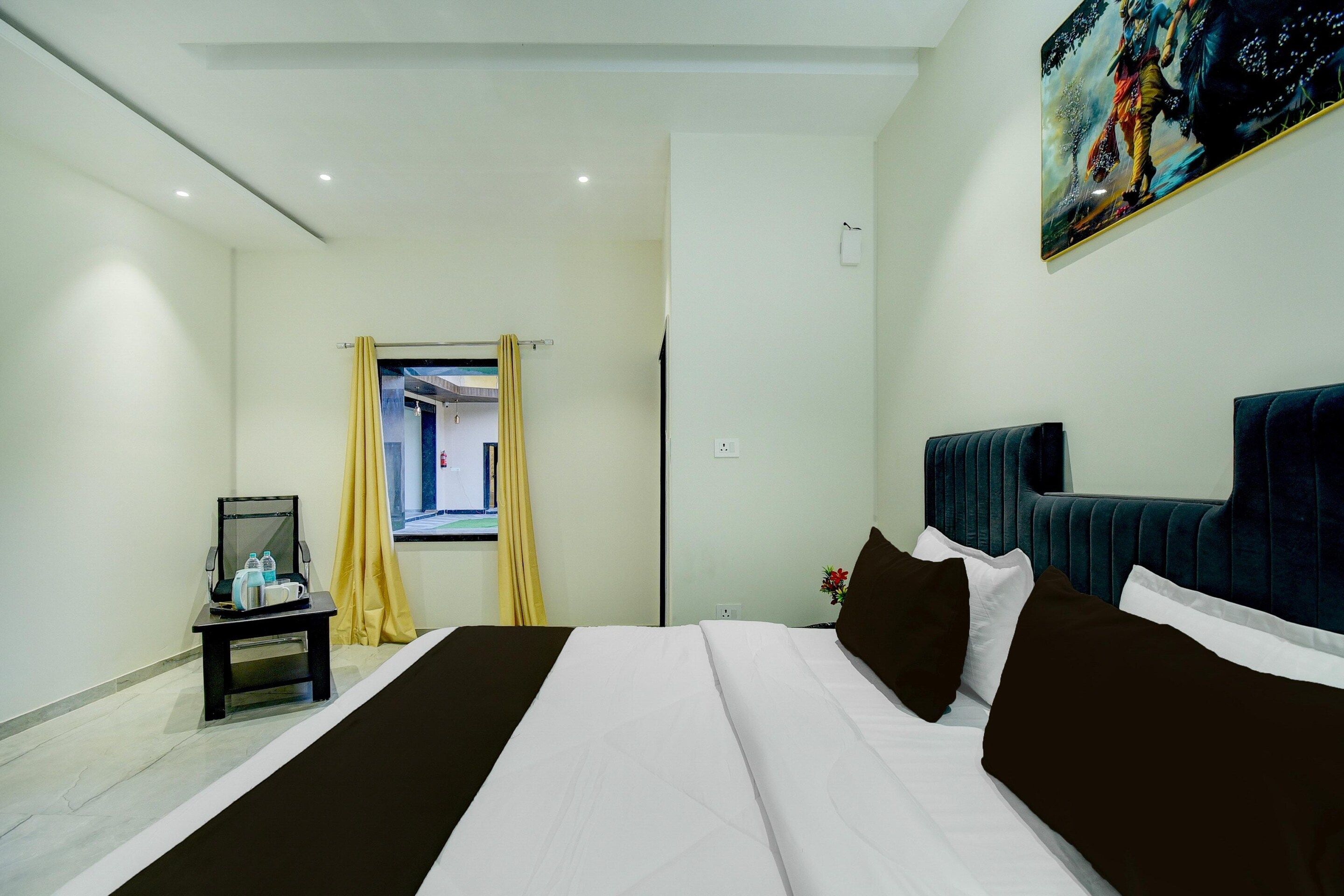 Una camera d'albergo con un letto, un comodino, una finestra con tende e un quadro appeso al muro.