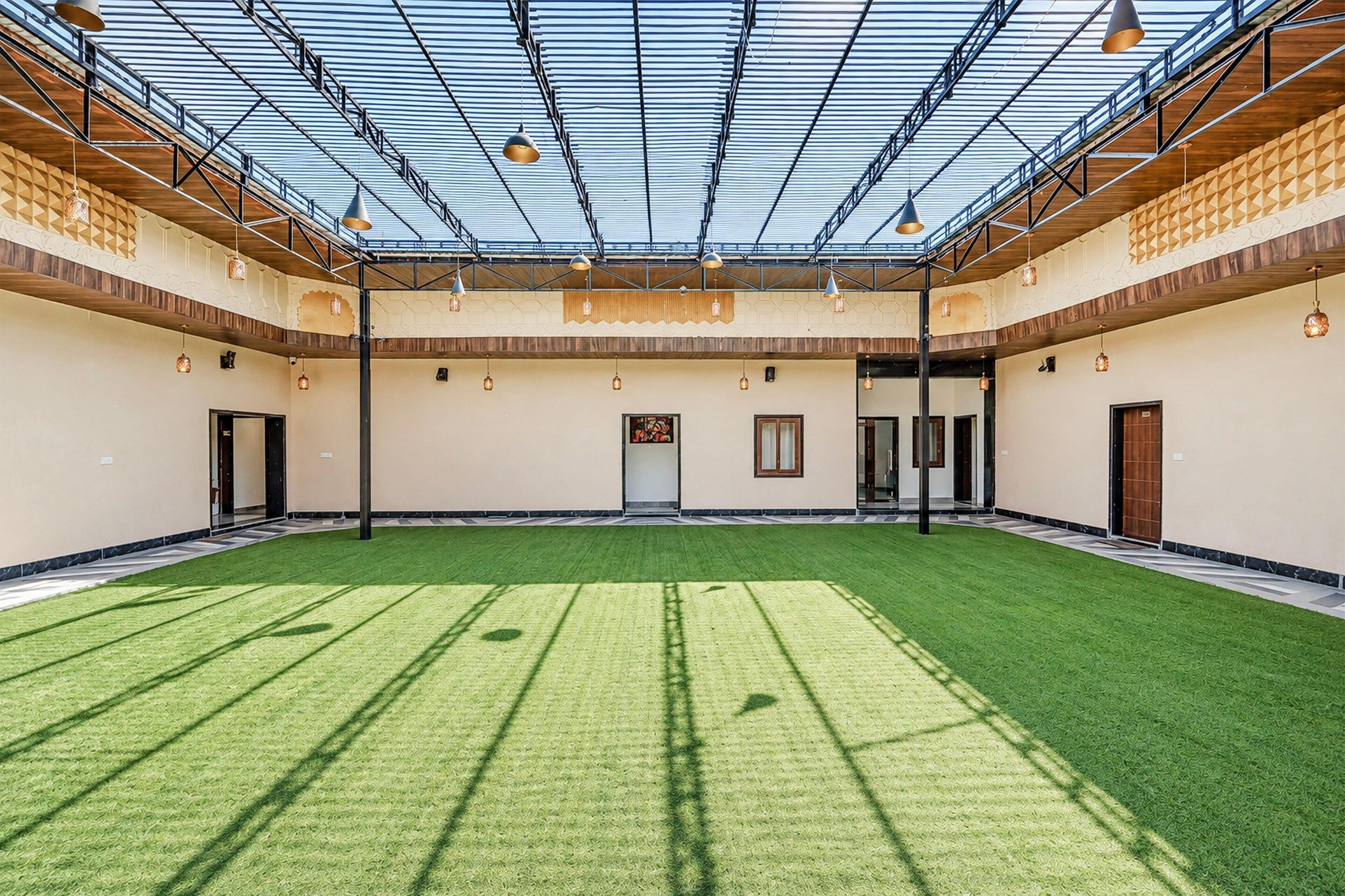 A spacious indoor area with a green artificial turf floor, a high ceiling with a glass roof, and multiple hanging pendant lights.
