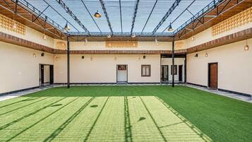A spacious indoor area with a green artificial turf floor, a high ceiling with a glass roof, and multiple hanging pendant lights.