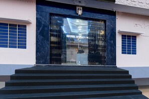 Entrada de un edificio con una escalera que conduce a una puerta de cristal con rejas de metal.