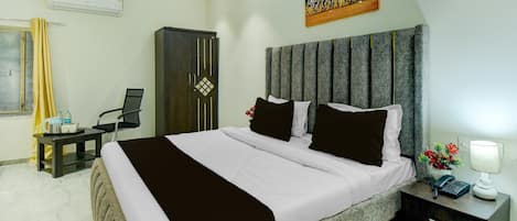 A hotel room with a bed, bedside table, nightstand, and a wall-mounted air conditioner.