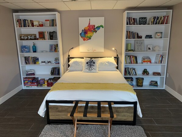 A bedroom with a bed, two bookshelves, a map, and a variety of books and decorative items.
