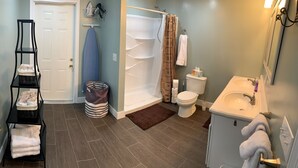 Un bagno con doccia, wc e lavandino. C'è uno scaffale con asciugamani e un cestino della spazzatura a righe.