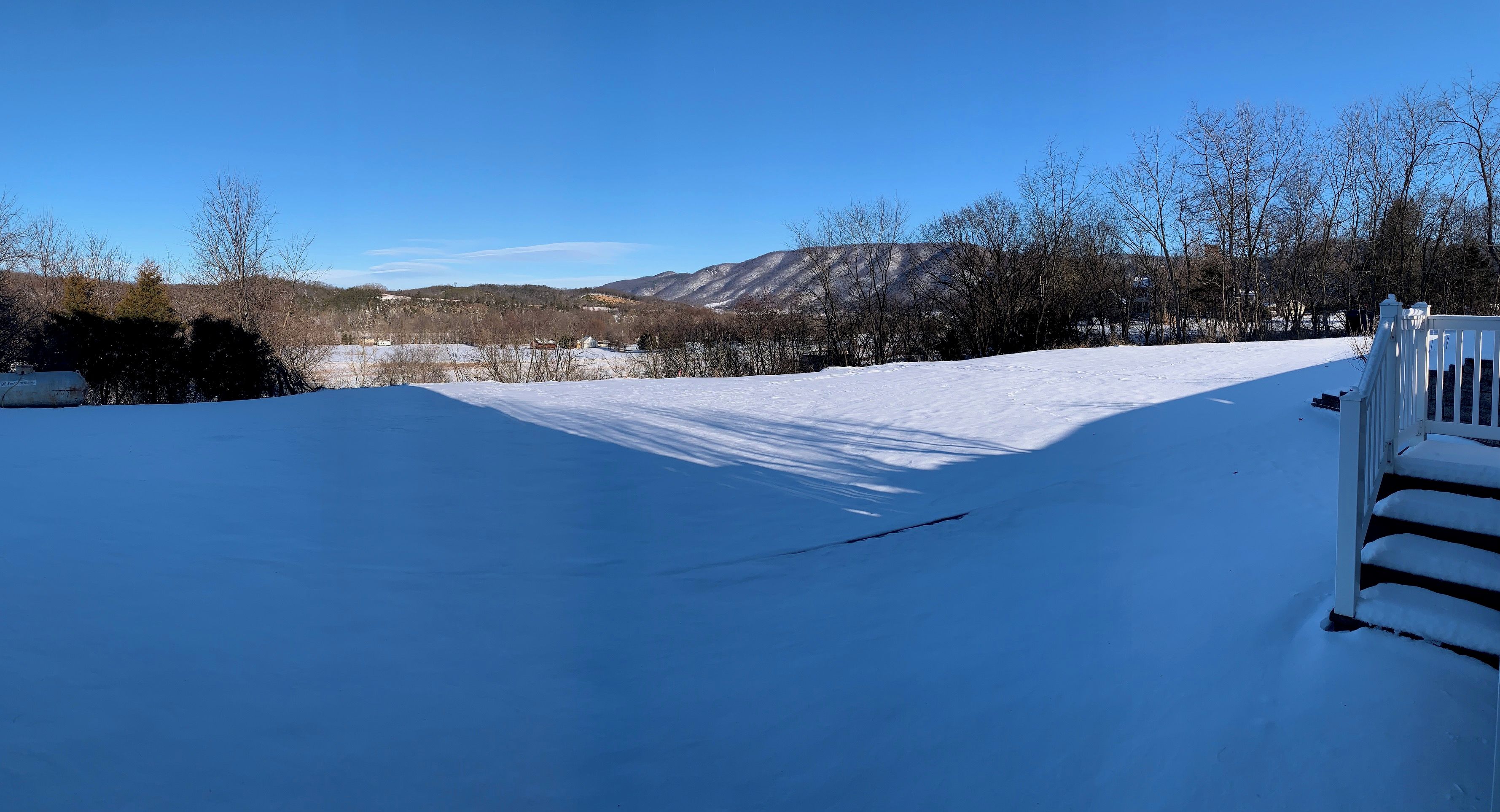 A snow-covered landscape with a clear sky, a wooden fence, and a distant view of mountains.