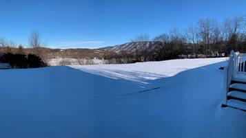 A snow-covered landscape with a clear sky, a wooden fence, and a distant view of mountains.