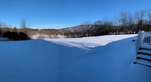 A snow-covered landscape with a clear sky, a wooden fence, and a distant view of mountains.
