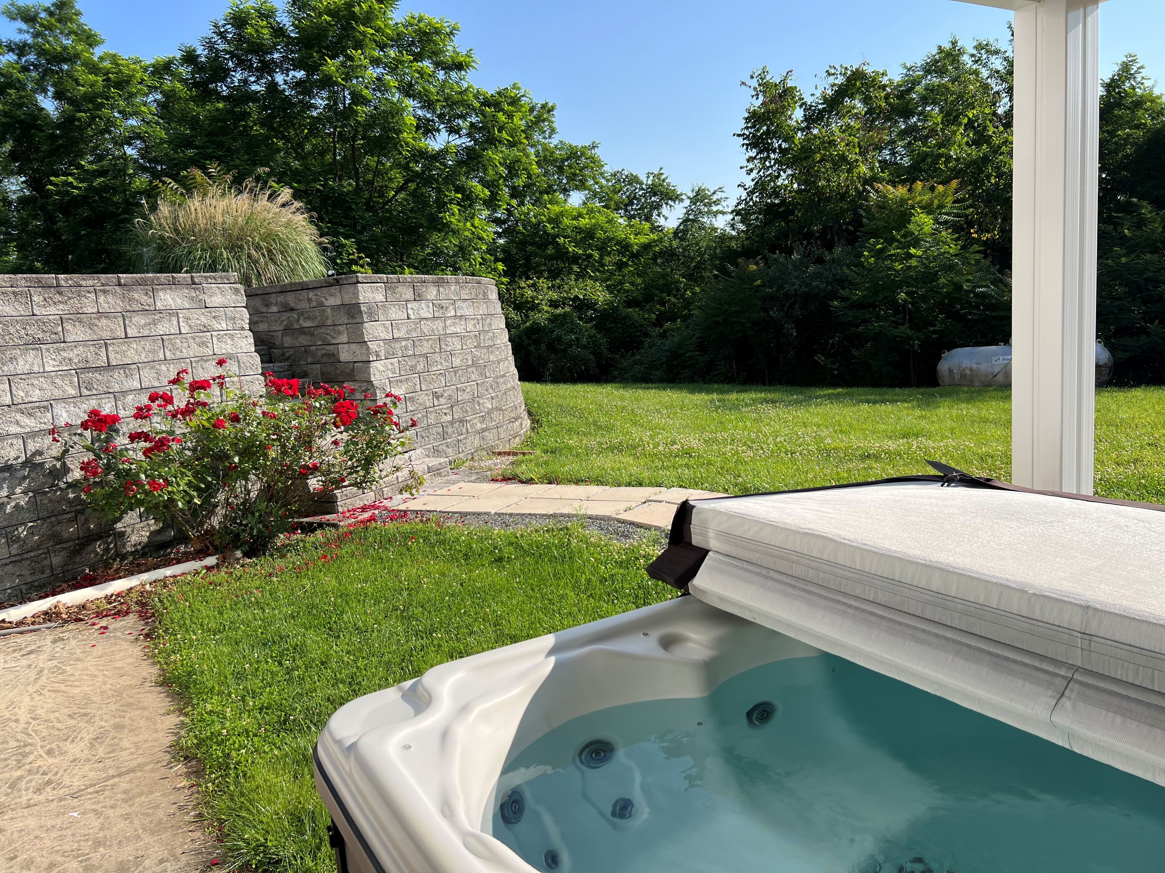 Un jacuzzi en un patio trasero con un muro de piedra y flores rojas.