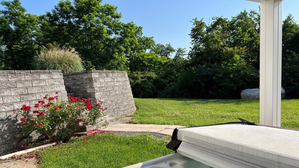 Una vasca idromassaggio in un giardino sul retro, con un muro in pietra e fiori rossi.