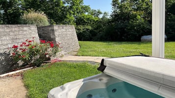 Un jacuzzi en un patio trasero con un muro de piedra y flores rojas.