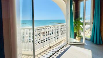 A balcony with a view of the sea, a potted plant, and a wooden ceiling.
