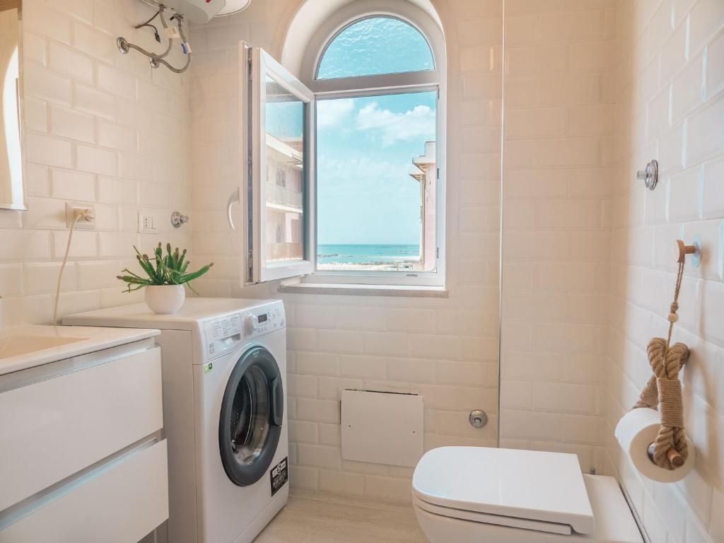 Un baño pequeño con lavadora, inodoro y ventana con vista a la playa.