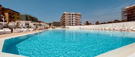 Una piscina con sillas de descanso y un edificio al fondo.
