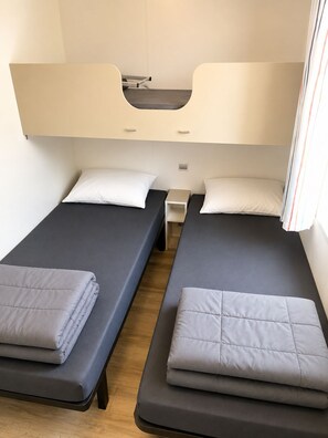 Una stanza con due letti, ognuno con un cuscino e una coperta piegata. C'è un comodino tra i letti.