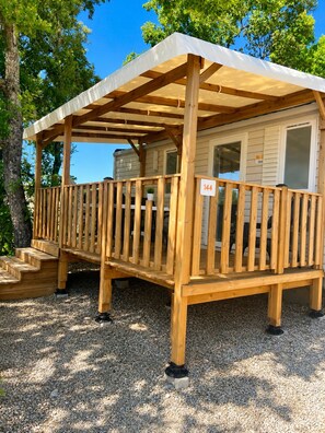 Un patio in legno con una tettoia, un numero e terreno sterrato.