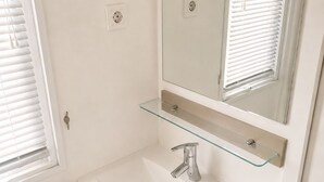 Een badkamer met een witte wastafel, een glazen plank, een spiegel en een handdoekhouder.