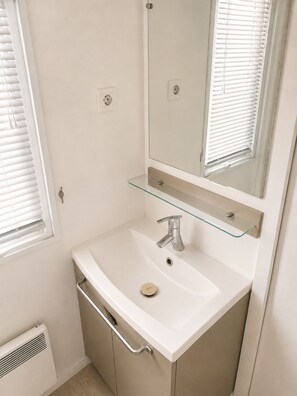Un bagno con un lavandino bianco, uno specchio e uno scaffale in vetro.