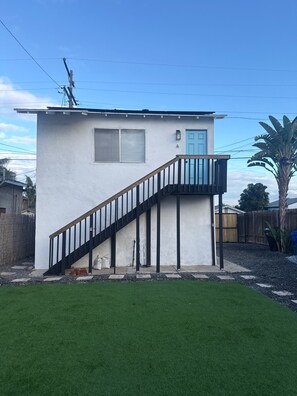A single-story building with a white exterior, a blue door, and a black staircase leading to a small balcony. - Cozy 1-bedroom apartment in marvelous San Diego with AC (San Diego)