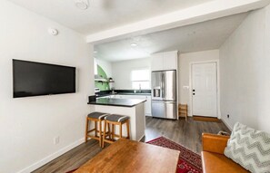 A modern kitchen with a built-in island, a flat-screen TV mounted on the wall, and a dining area with a wooden table and bar stools. - Cozy 1-bedroom apartment in marvelous San Diego with AC (San Diego)