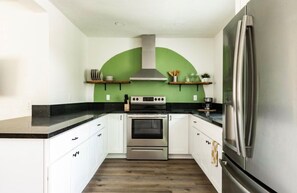 A kitchen with white cabinets, a stainless steel refrigerator, a double oven, and a green accent wall. - Cozy 1-bedroom apartment in marvelous San Diego with AC (San Diego)