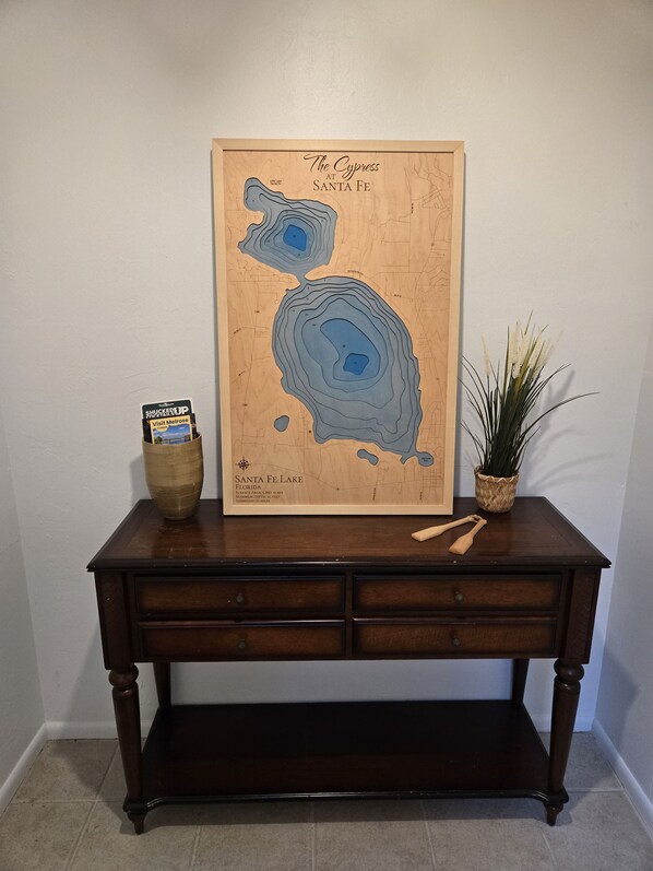 A wooden map of Santa Fe Lake, Florida, on a dark wooden table with a plant and a small basket. - Lake Santa Fe Getaway | Private Dock + Kayaks (Melrose)