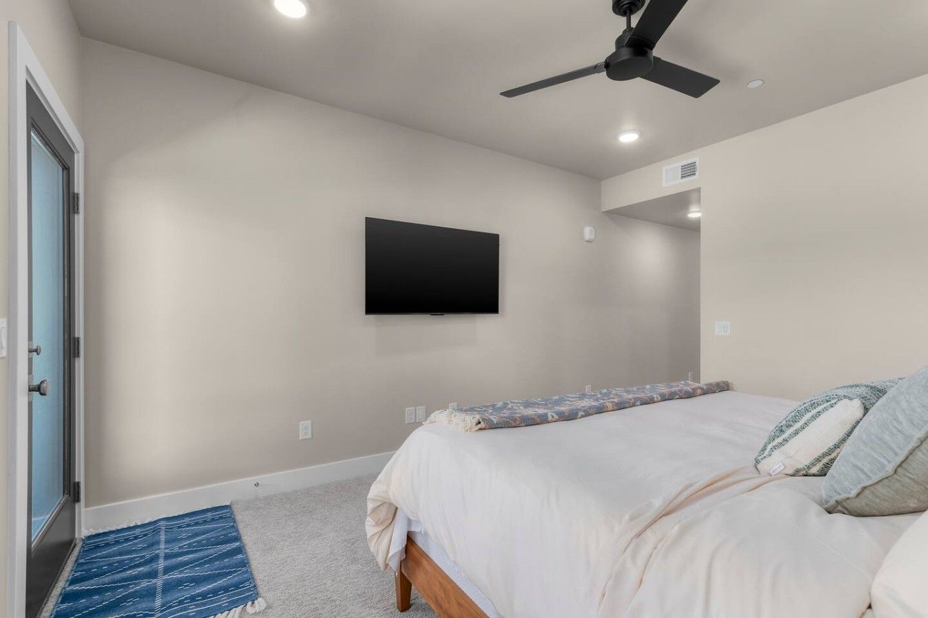 Un dormitorio con cama, ventilador de techo, televisor montado y una puerta.