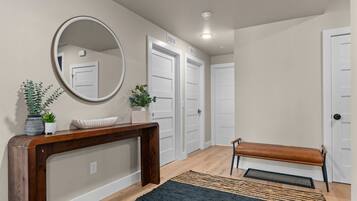 A hallway with a wooden console table, a bench, a mirror, and two doors.