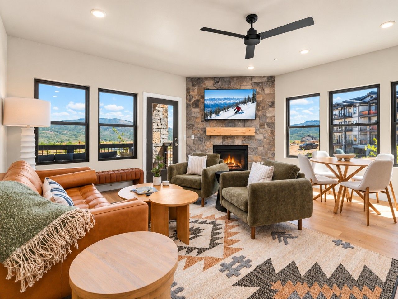A modern living room with a fireplace, comfortable seating, large windows, and a mountain view.