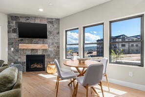 A modern living room with a stone fireplace, a flat-screen TV, and a dining area with a table and chairs. - Deer Valley East 3BR•Hot Tub•Pool•Lake View (Heber City)