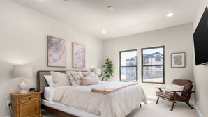 Une chambre à coucher avec un lit, une table de chevet, une lampe et une fenêtre donnant sur un immeuble.