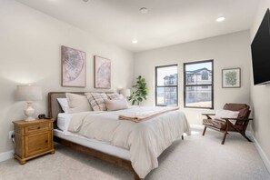 A bedroom with a bed, bedside table, lamp, and a window with a view of a building. - Deer Valley East 3BR•Hot Tub•Pool•Lake View (Heber City)