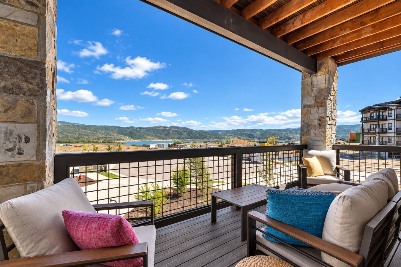A balcony with a view of a lake and mountains, furnished with a sofa and chairs.