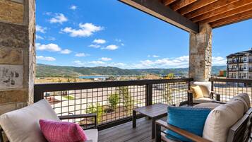A balcony with a view of a lake and mountains, furnished with a sofa and chairs.