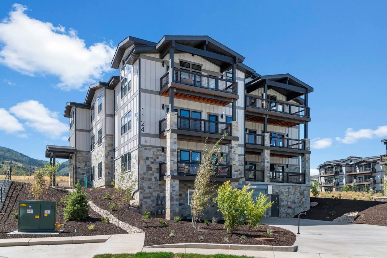 A multi-story residential building with balconies, stone facade, and a clear sky.