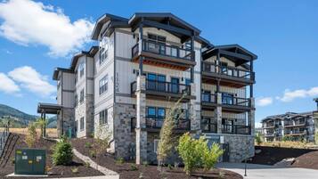 A multi-story residential building with balconies, stone facade, and a clear sky.