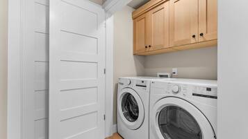 A laundry room with two front-loading washing machines, wooden cabinets above, and a white door.